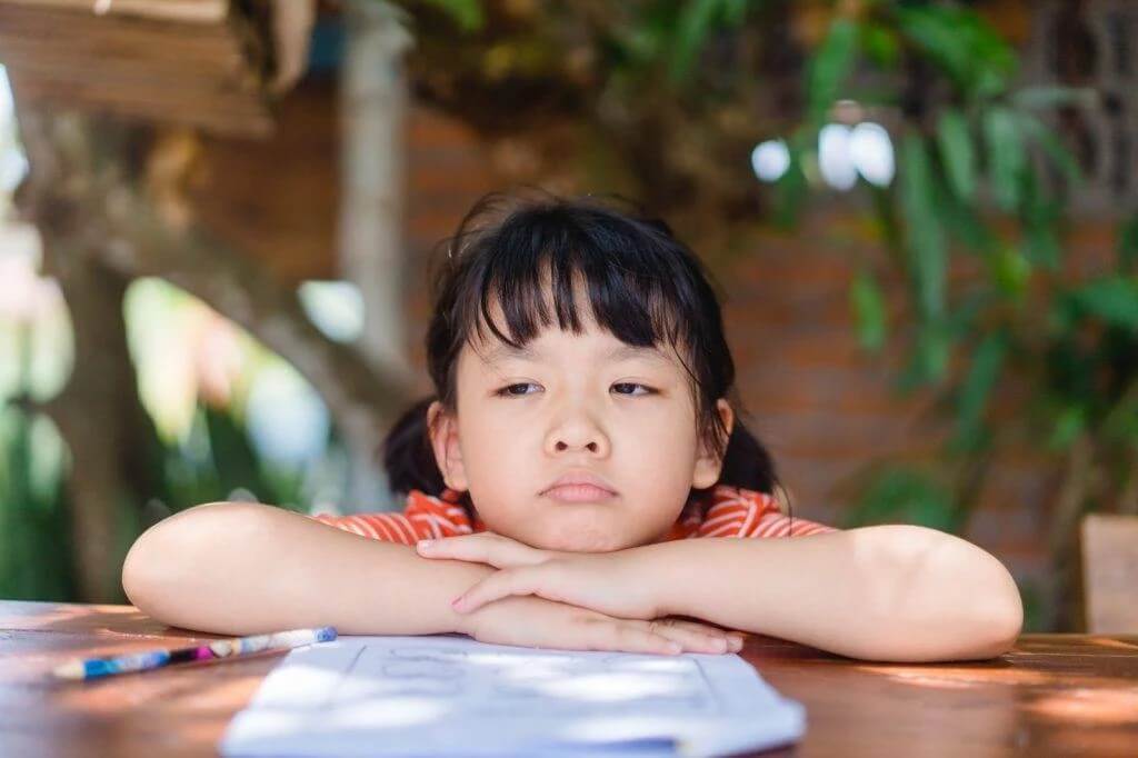 Em nhỏ ngồi chống tay với biểu hiện buồn và suy nghĩ nhiều, minh họa tình trạng trẻ thiếu tự tin và ngại thể hiện cảm xúc